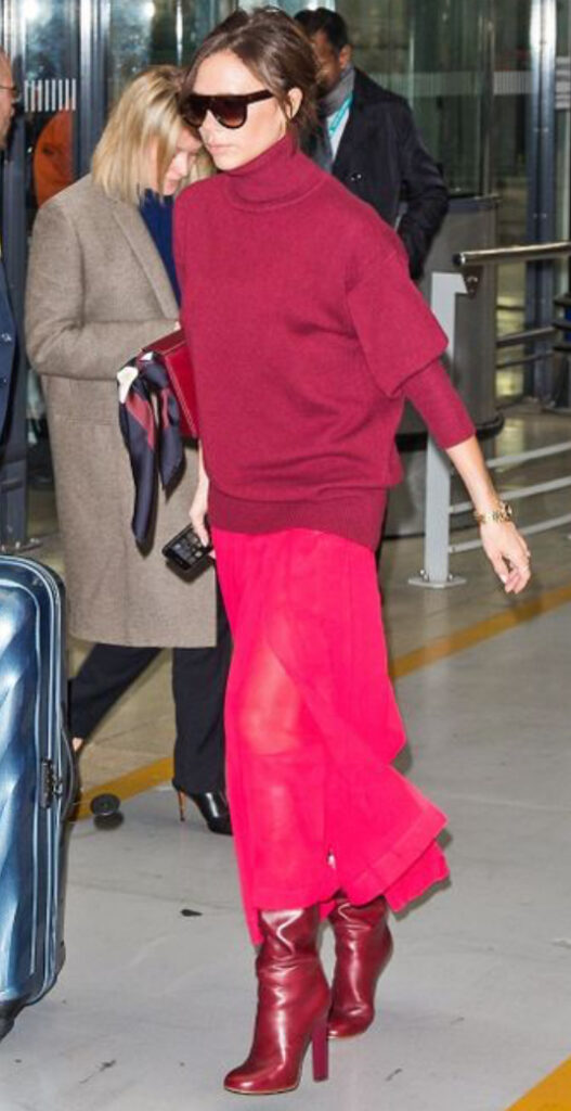 victoria beckam con un outfit con gonna, maglione e stivali. tutto di diverse gradazioni di bordeuax 