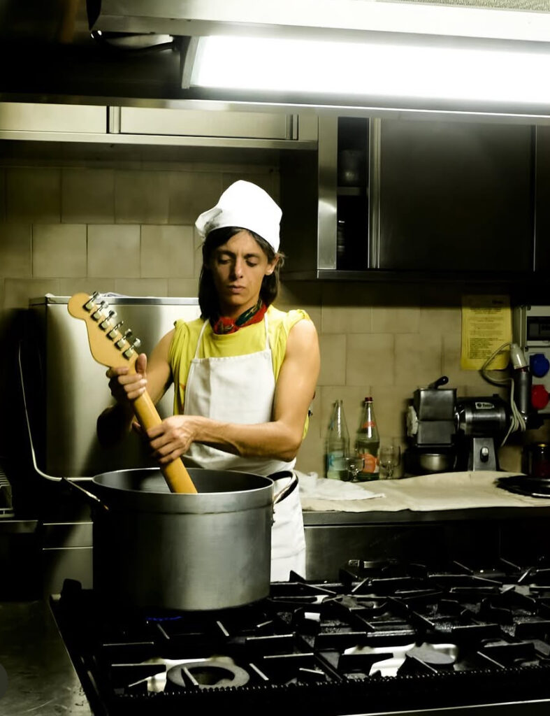 Lucio Corsi in una cucina con la chitarra dentro una pentola. Oltre a chi è joan thiele ci siamo chiesti anche chi sia lucio corsi