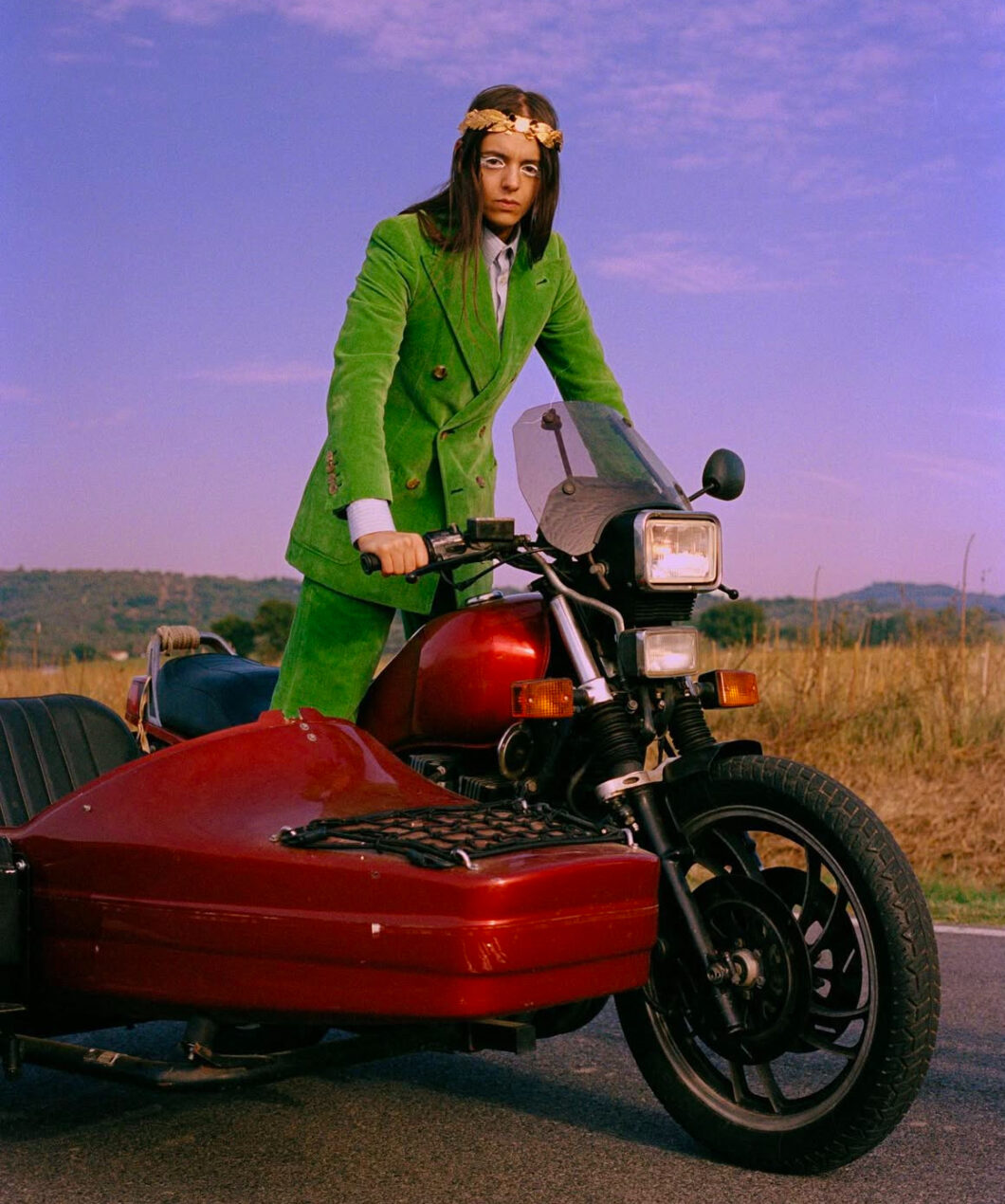 Lucio Corsi fenomeno di Sanremo in piedi su un sidecar con vestito verde di Gucci