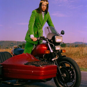 Lucio Corsi fenomeno di Sanremo in piedi su un sidecar con vestito verde di Gucci