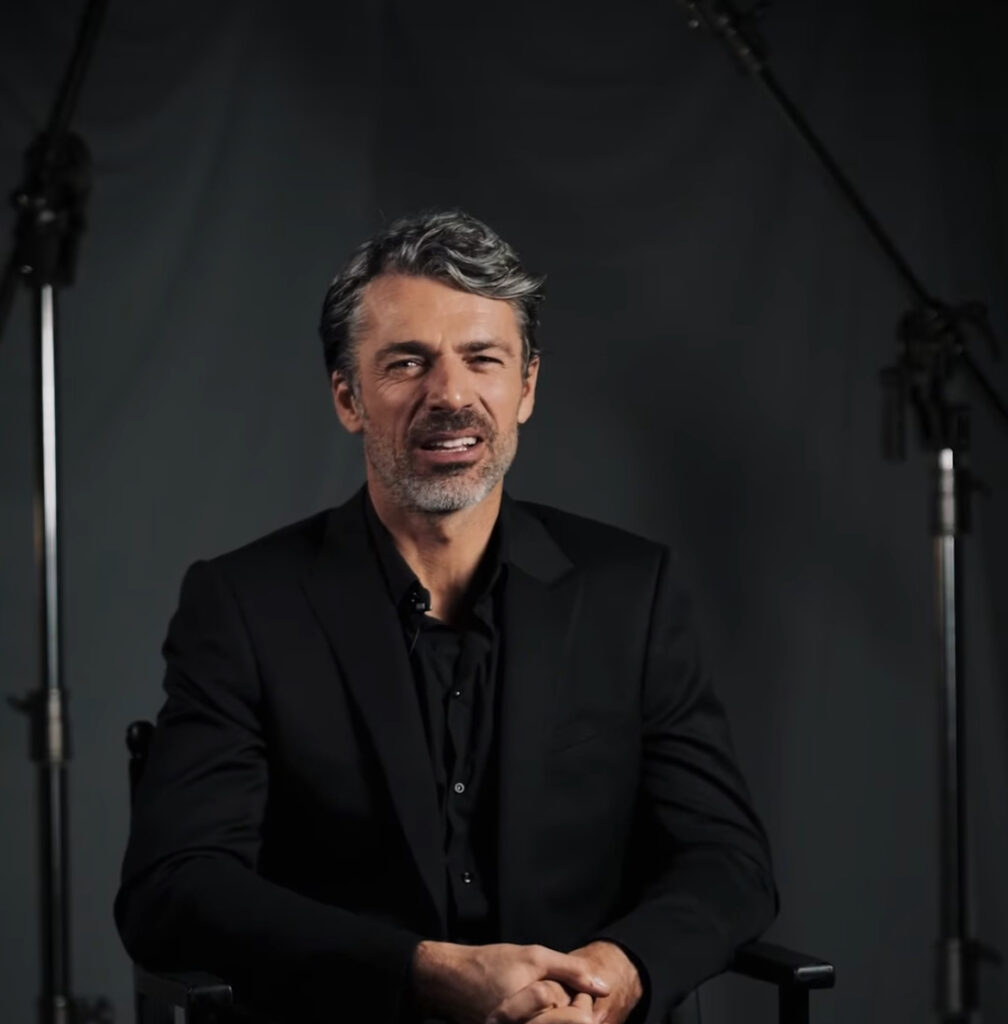 Luca Argentero durante un'intervista con un vestito nero e il ciuffo. Capelli tiratidi Prodi e altri sfatti.